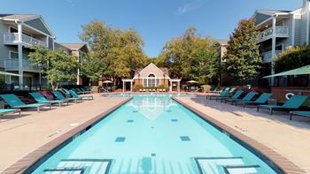 A swimming pool with blue chaise lounge chairs and a house in the background